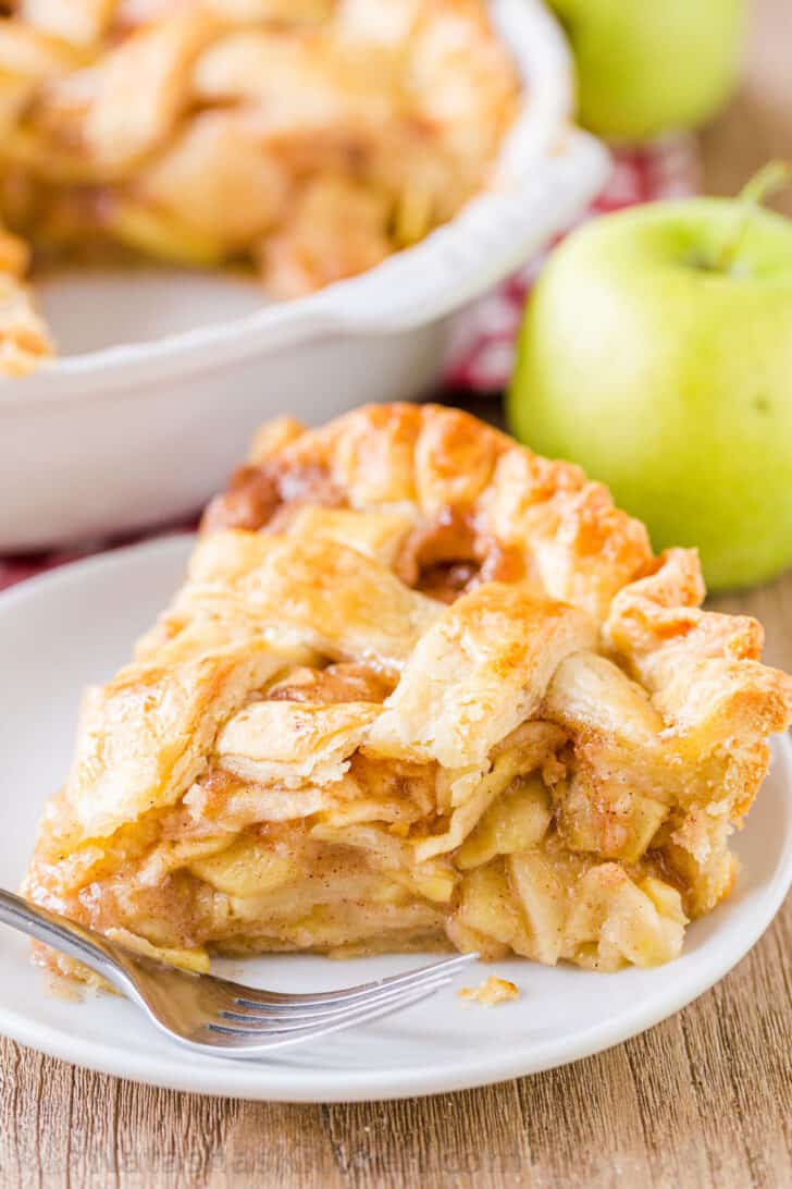 Apple pie slice on a plate with apples in background