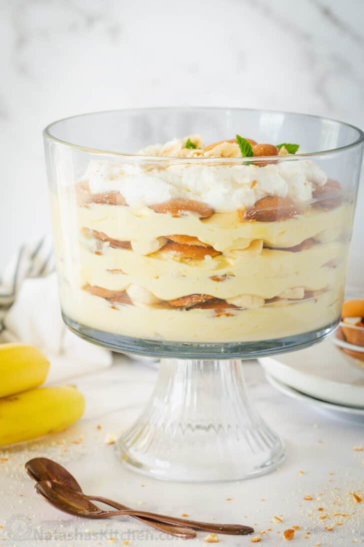 A trifle bowl with banana pudding layered and bananas on the side of the bowl.
