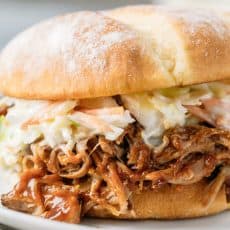 BBQ pulled pork with coleslaw on a bun served on a plate.