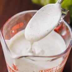 A spoon drizzles ranch dressing into a measuring cup.