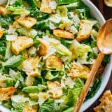 Caesar Salad recipe in a bowl with romaine, croutons, parmesan cheese and caesar dressing