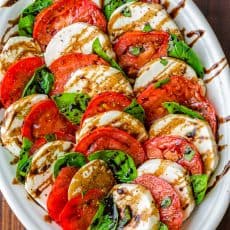 Caprese salad assembled on white platter drizzled with balsamic glaze