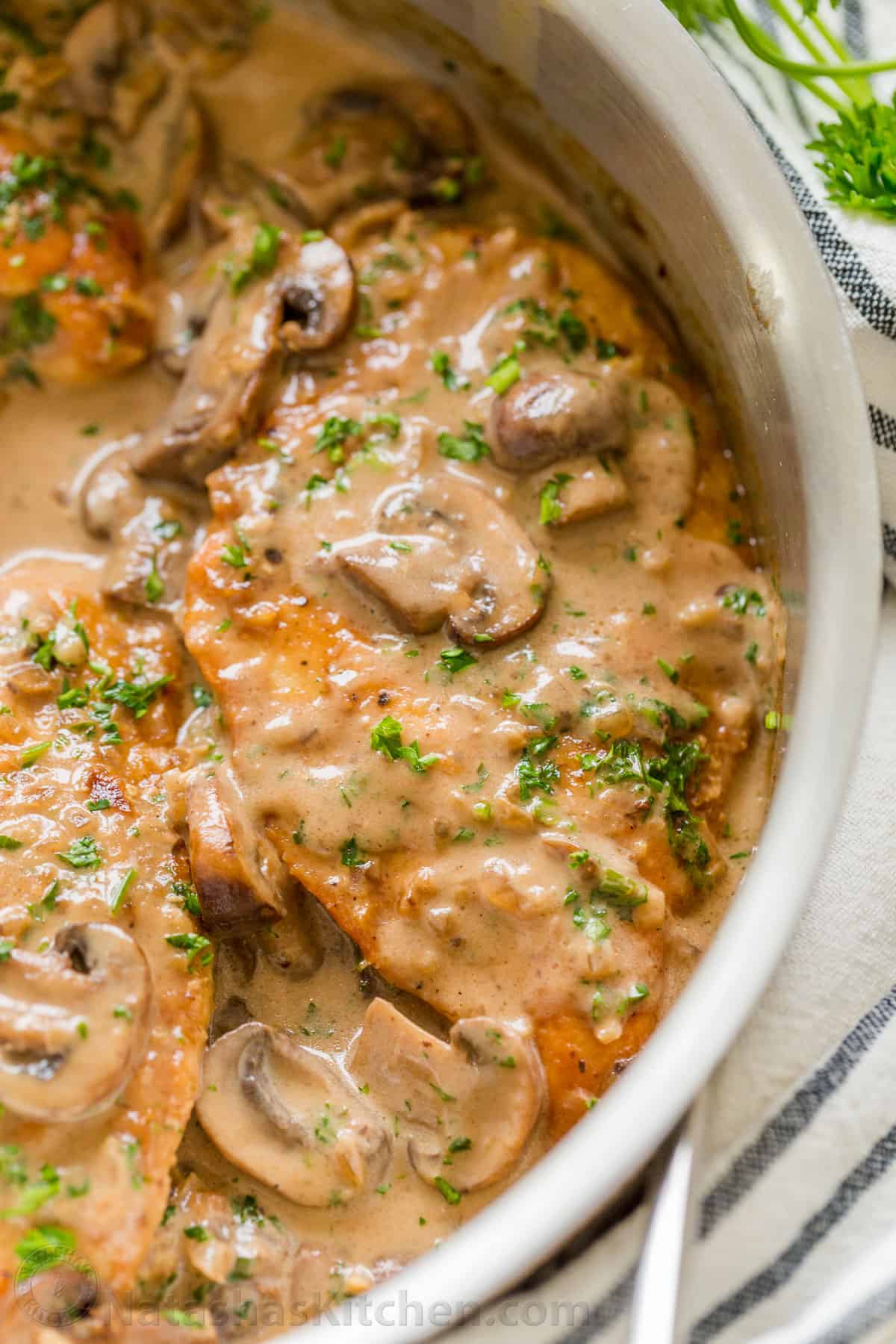 Close-up of Chicken Marsala topped with mushrooms and parsley in a pan