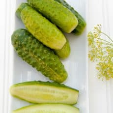Pickles on a long tray with a piece of dill besides them