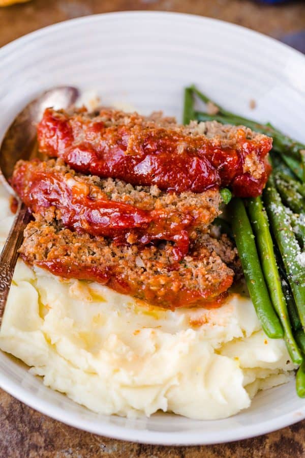 Meatloaf recipe sliced and served on a plate with mashed potatoes and vegetables