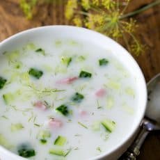 A bowl of Okroshka Summer Soup with dill and a spoon next to the bowl.