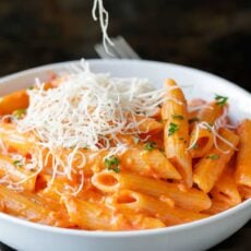 A bowl of homemade penne alla vodka topped with grated parmesan cheese and fresh herbs.