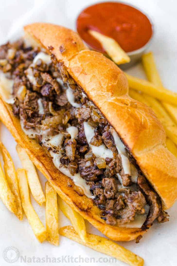 Philly cheesesteak sandwich served in a bun with fries and ketchup