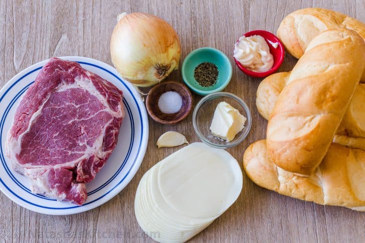Ingredients for philly cheesesteak sandwich including ribeye steak, hoagie rolls, provolone cheese, onion, mayo, garlic butter