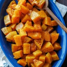 Roasted butternut squash on a blue oval platter with a serving spoon.