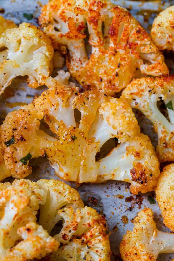 Sliced cauliflower steaks roasted in butter and seasoning on a baking sheet. 