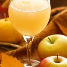 A wine glass with Russian apple kvas and full apples beside the glass