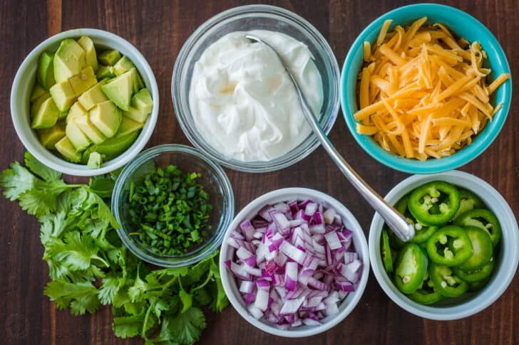 Toppings for chili with avocados, chives, onion, jalapeños, cheese, sour cream and cilantro