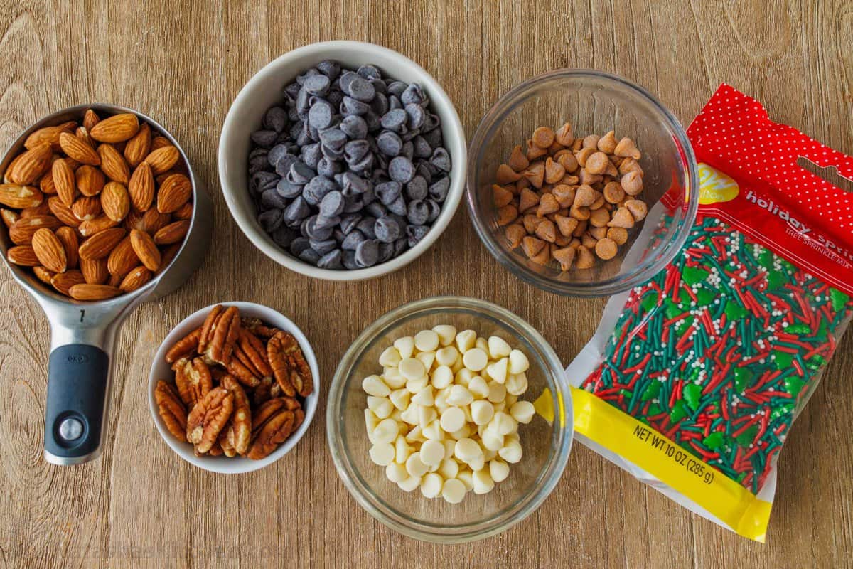 Toppings for holiday candy such as almonds, butterscotch chips, white chocolate chips, chocolate chips, pecans and holiday sprinkles
