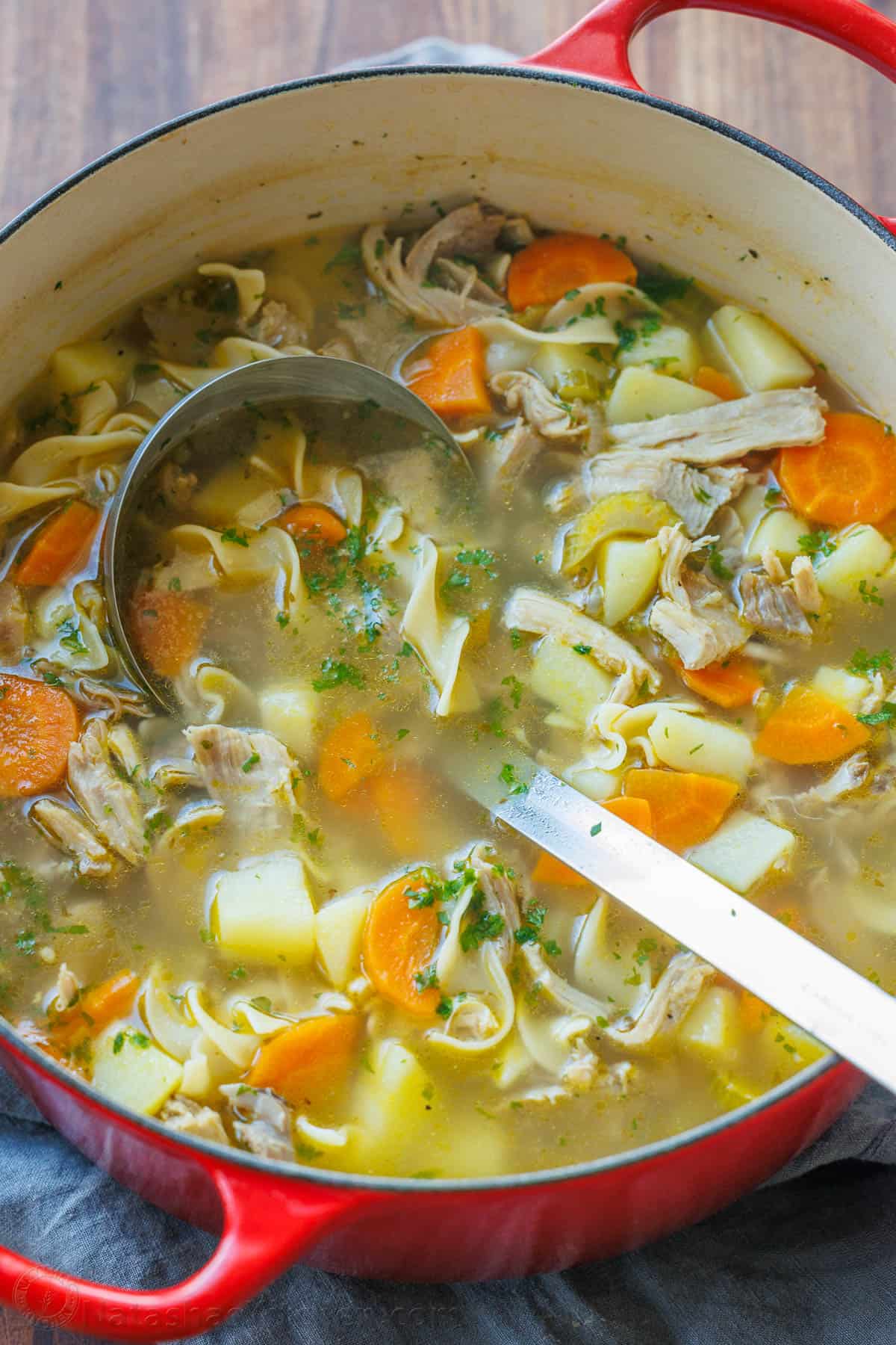 Hearty turkey noodle soup being scooped out of a pot with a large ladle