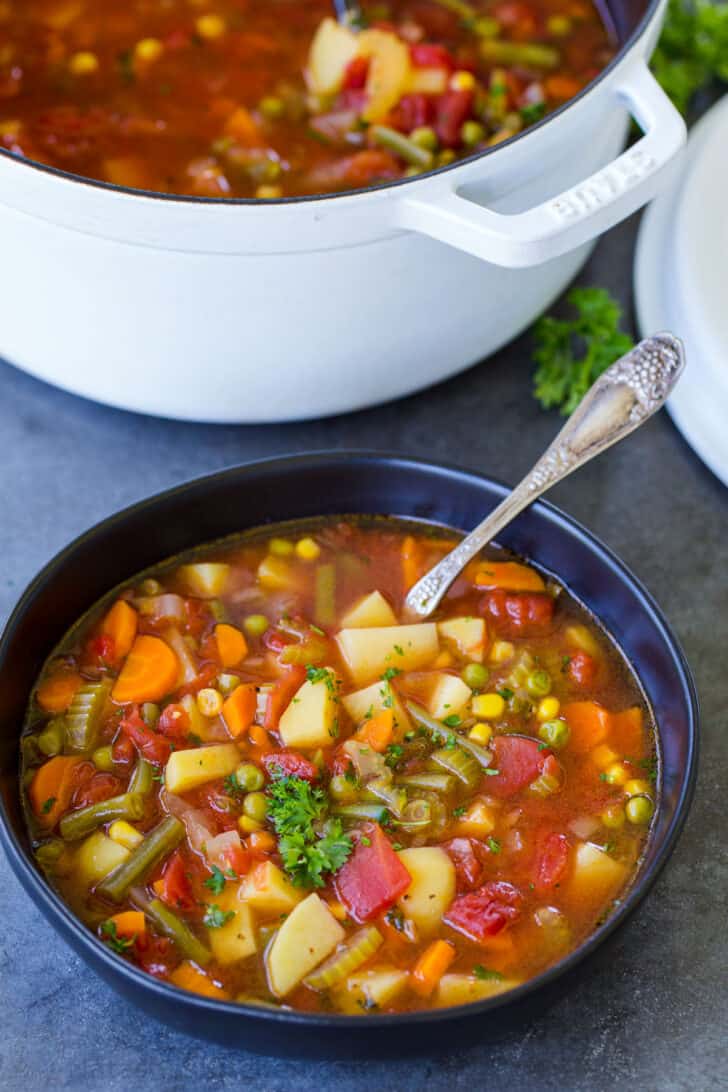 A bowl of vegetable soup next to the pot