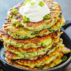 Stack of zucchini fritters topped with sour cream and scallions